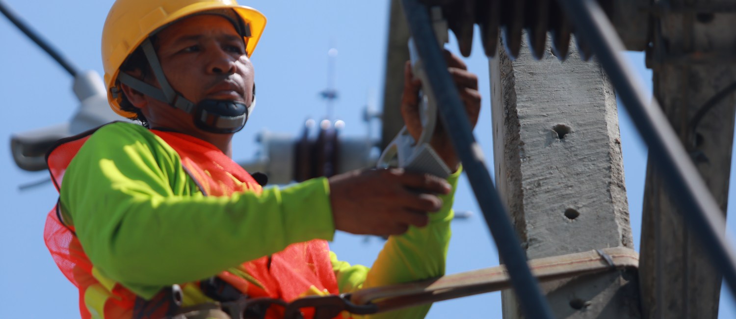 A man in a yellow helmet is working on a power line